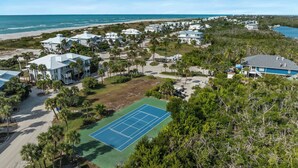 Un quartier résidentiel situé sur la côte, avec plusieurs maisons, un court de tennis et une plage en arrière-plan.