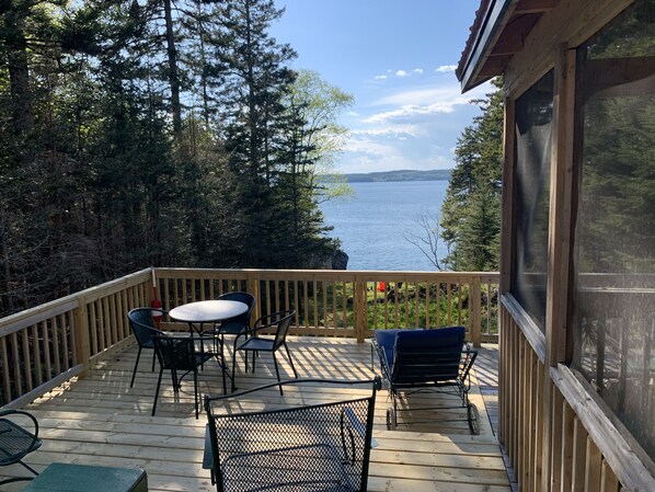 Una terraza de madera con mobiliario exterior, con vistas a un lago rodeado de árboles.