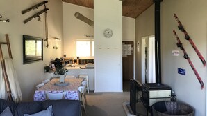A cozy living room with a fireplace, a dining area, and a kitchen visible through an open door. - Yowie 3 - (Yowie Lodge) (Jindabyne)