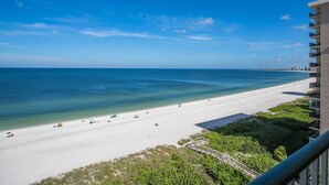 Blick auf einen Strand vom Balkon, über einem Sandstrand mit blauem, wolkenlosem Himmel.