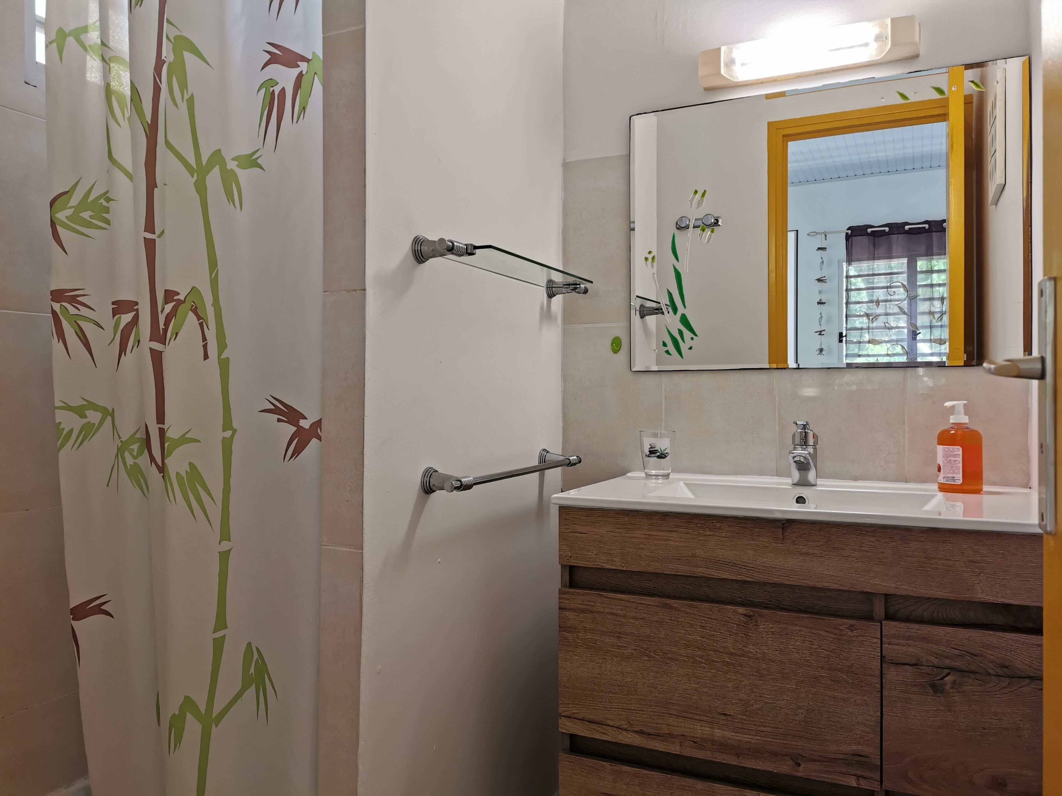 Un baño con cortina de ducha de estilo bambú, un espejo con marco amarillo, un lavabo con dispensador de jabón y armarios de madera.