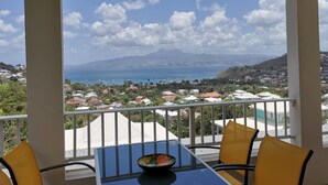 A balcony with a table and chairs, overlooking a coastal town with houses and a mountain in the distance. - Hibiscus: calm and breathtaking views for this T3 overlooking the bay of Fort de France (Les Trois-Îlets)