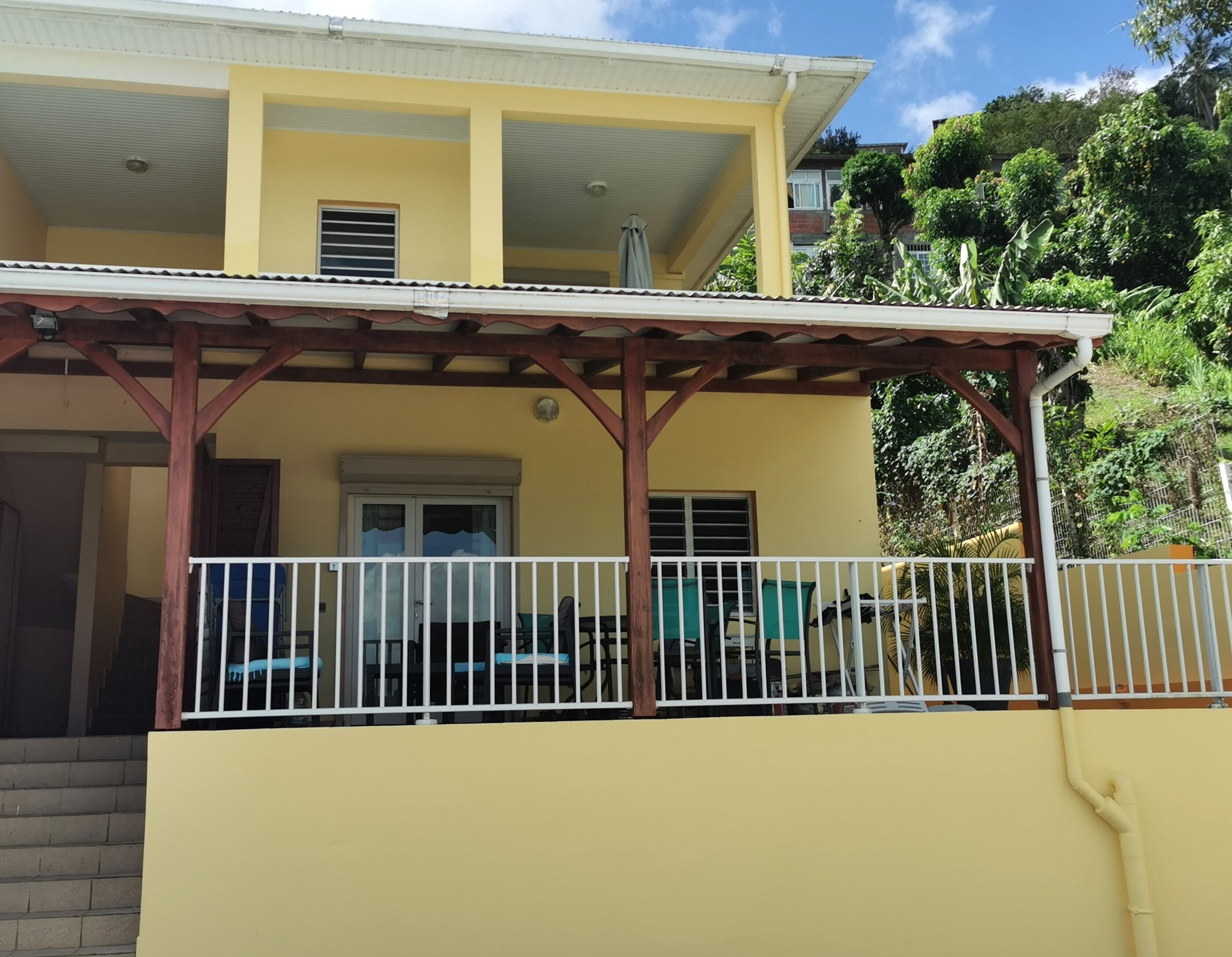 A two-story building with a yellow facade, a covered porch with a white railing, and a staircase leading to the entrance.