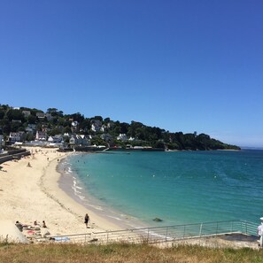 Uma praia com areal dourado, águas azul-claras e casas numa encosta ao fundo.