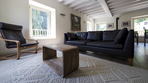A living room with a dark leather sofa, a wooden coffee table, and a patterned rug. There is a window with a view of trees and a painting on the wall. - an oasis of relaxation in the quiet of Valpantena (Grezzana, Verona)