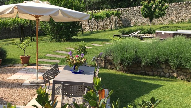 A patio with a table, chairs, and a white umbrella. There are potted plants and a stone wall in the background. - an oasis of relaxation in the quiet of Valpantena (Grezzana, Verona)