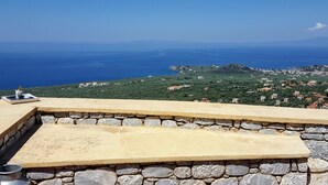 Un banco de piedra con vistas a un paisaje costero, donde se aprecia el mar y edificios lejanos.