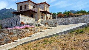 Una casa de piedra con techo de tejas, una escalera de piedra y un paisaje montañoso de fondo.