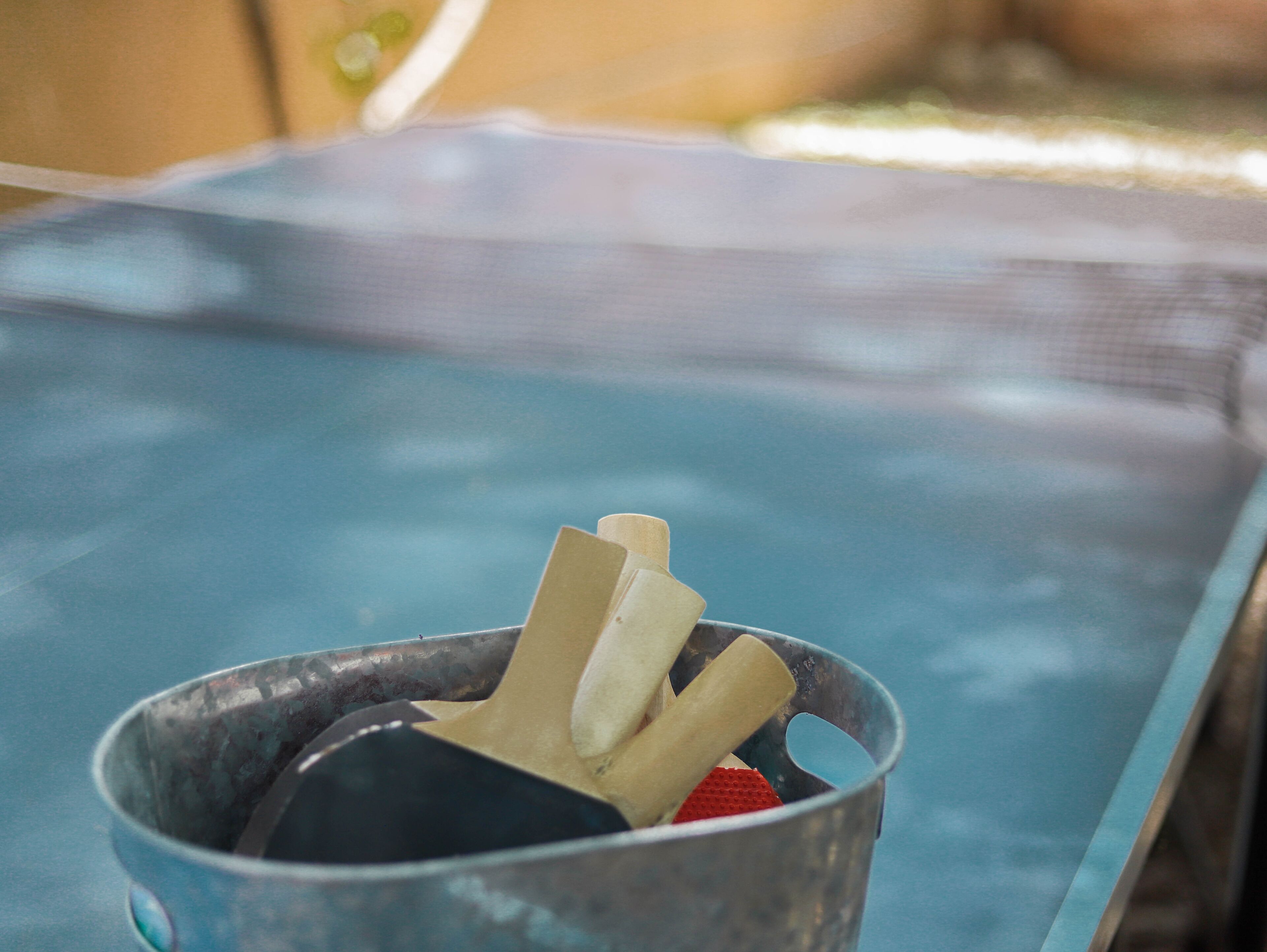 A metal bucket with a red object and a black object inside, placed on a blue surface.