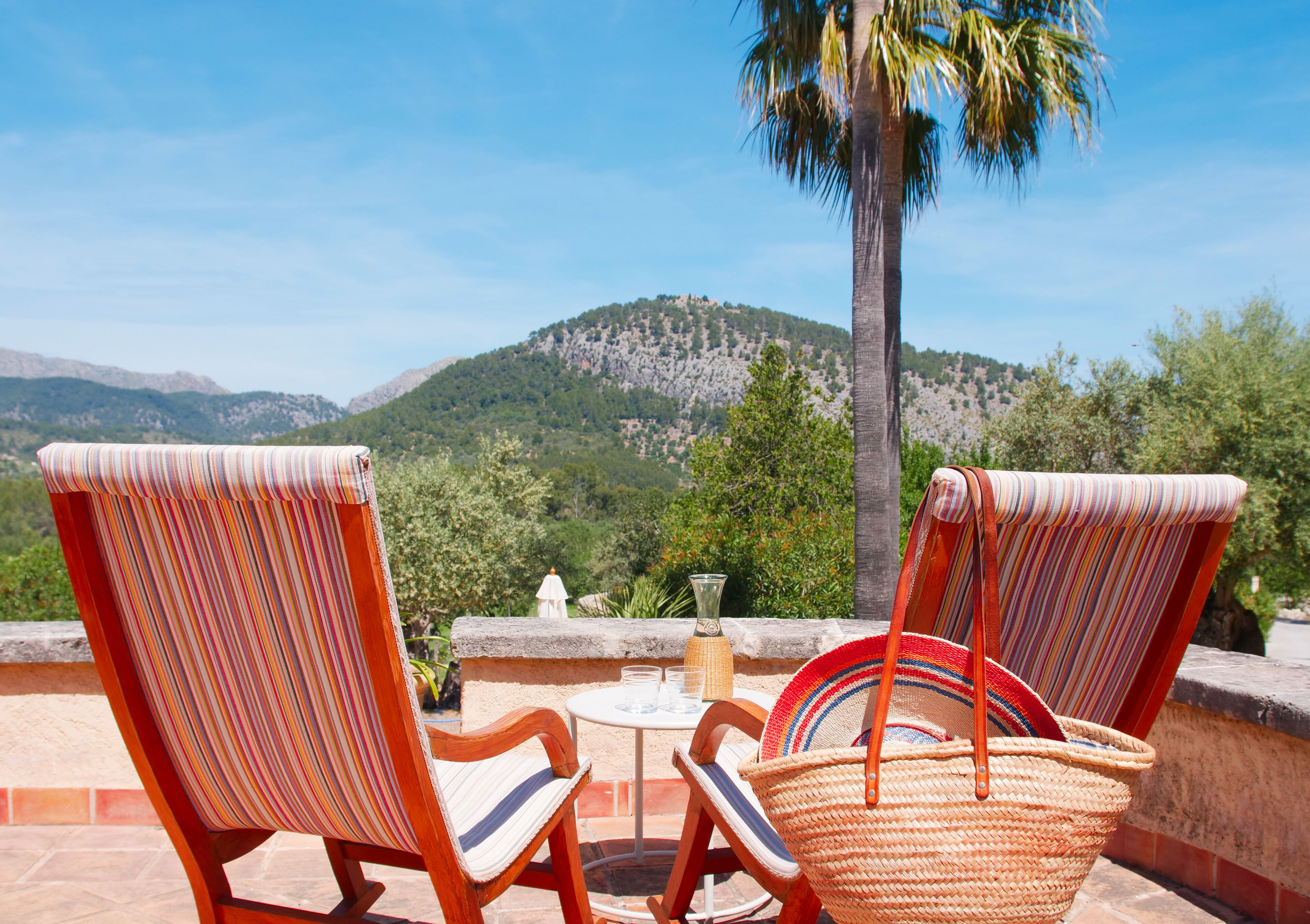 Two striped lounge chairs facing a scenic mountain view with a palm tree.