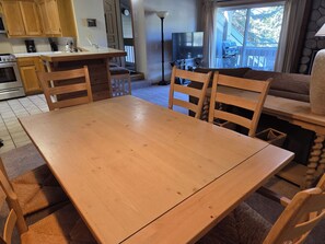 A dining area with a wooden table and chairs, a kitchen with wooden cabinets, a TV, and a view of the outdoors.