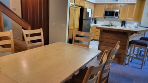 Une table de salle à manger en bois avec des chaises, une cuisine avec des meubles en bois, un réfrigérateur en acier inoxydable et un four à micro-ondes.