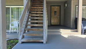 A wooden staircase leading to a door with a decorative glass panel, surrounded by a balcony with railings.