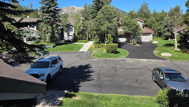 A residential street with houses, a driveway, and a mountain in the background.