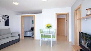 A modern living room with a sofa, a dining area with a table and chairs, a TV, and a painting on the wall. - Alexis plus Zeus Salou 0141 (Salou)