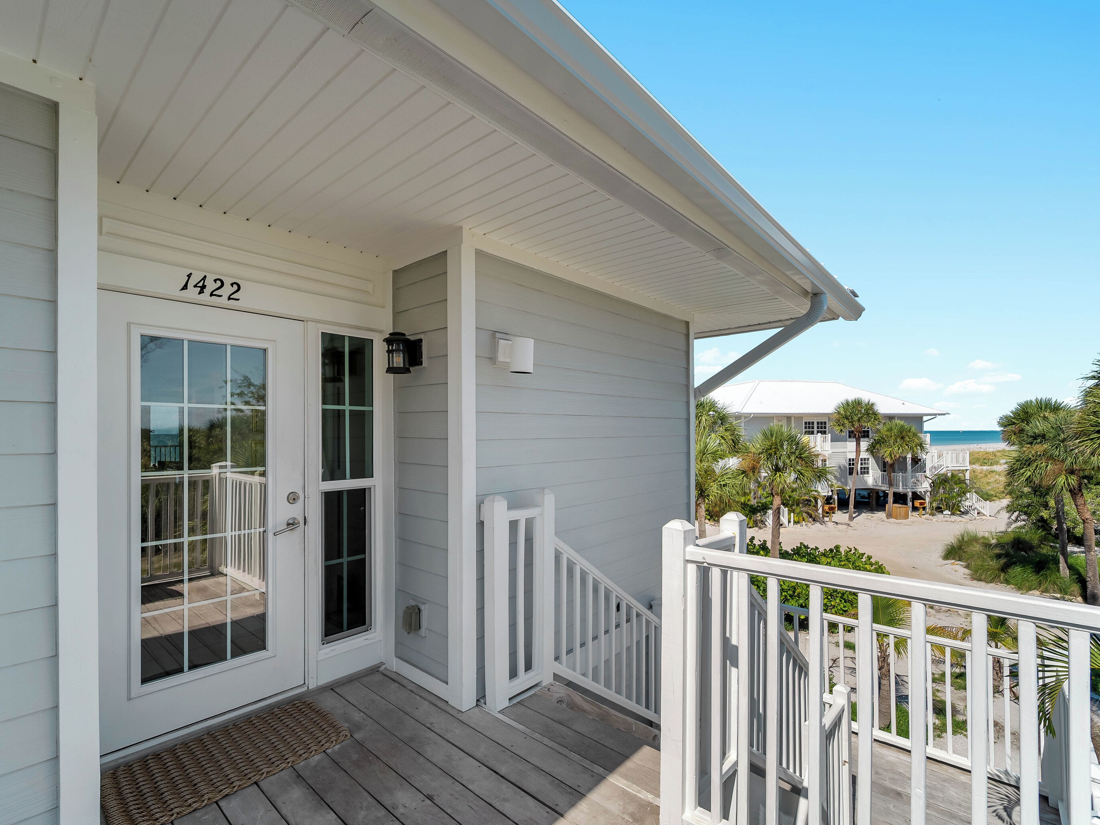 A coastal house with a white exterior, a front door with glass panels, and a balcony with a white railing.