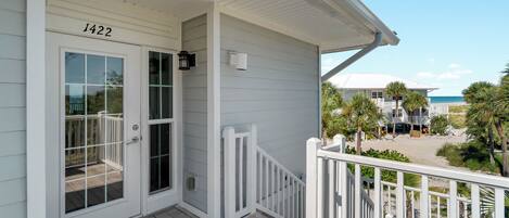A coastal house with a white exterior, a front door with glass panels, and a balcony with a white railing.