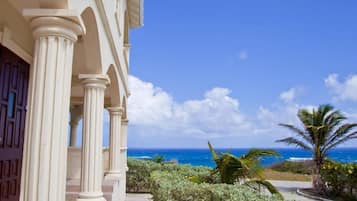 Un edificio con columnas clásicas, vista al océano y vegetación tropical.