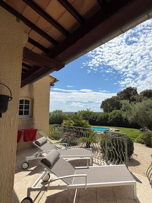 A covered outdoor area with lounge chairs, a pool, and a view of the landscape.