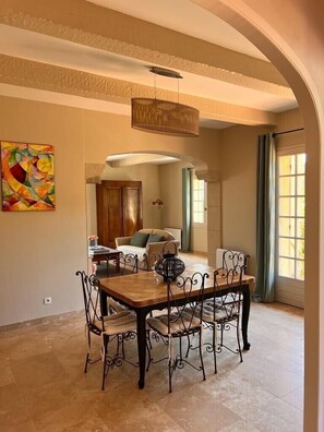 A dining area with a wooden table and metal chairs, a hanging light fixture, and a colorful abstract painting on the wall. - L'Oliveraie - Charming villa with a private pool and landscaped garden near Uzès (Montaren-et-Saint-Médiers)