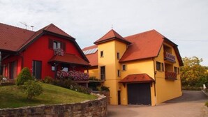 A two-story building with a red and yellow facade, a stone wall in front, and a paved driveway.