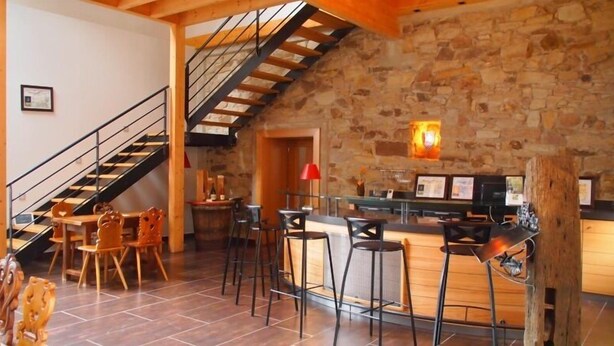 A rustic interior with a stone wall, wooden staircase, and a bar area with stools.