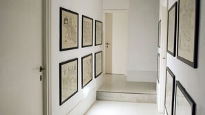 A hallway with framed artwork on the walls, a door on the left, and a staircase leading to another room. - Beautiful villa overlooking the sea in the Maremma National Park (Talamone)