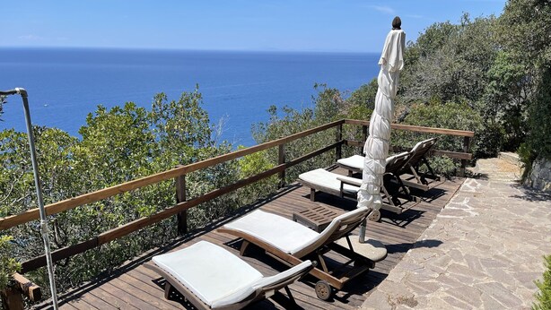 A wooden deck with lounge chairs and a table, overlooking a body of water. - Beautiful villa overlooking the sea in the Maremma National Park (Talamone)