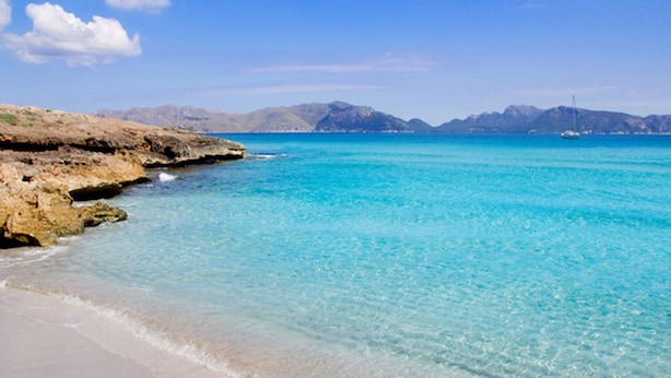 A beach with clear turquoise water, sandy shore, and rocky outcrops.