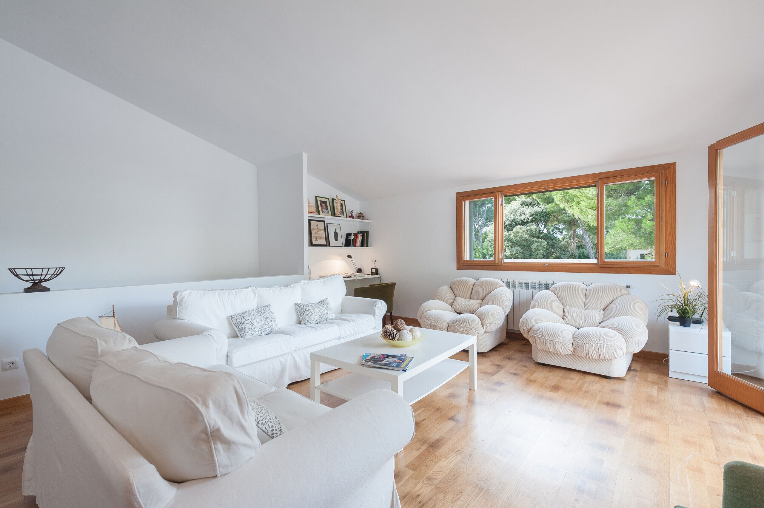 Una sala de estar moderna con un sofá blanco, una mesa de centro y una ventana con vistas a árboles.
