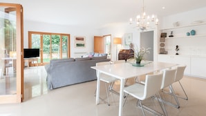 A modern living room with a grey sofa, a dining table with chairs, a TV, and a chandelier.