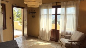 A room with a wooden ceiling, a round woven rug, a chair, and a view through a window with curtains. - Villa Pegasus Private pool villa ideal for a romantic get-away (Skopelos)