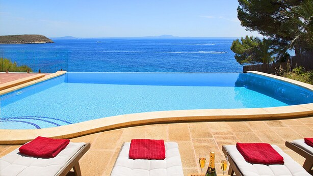 A pool with a view of the sea, lounge chairs with red towels, and a bottle of champagne.