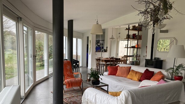 A spacious living room with a large sofa, a dining area, and a view through large windows. - Large modern villa surrounded by olive trees, , 20 minutes to Rome          (Sacrofano)