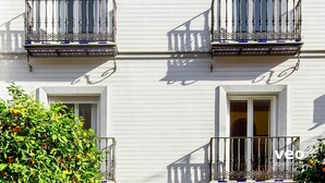 A building with white exterior walls, two balconies with ornate metal railings, and windows with white frames. - Studio in Macarena (Sevilla)