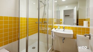 A bathroom with a glass-enclosed shower, a white sink, and yellow-tiled walls. - Studio in Macarena (Sevilla)