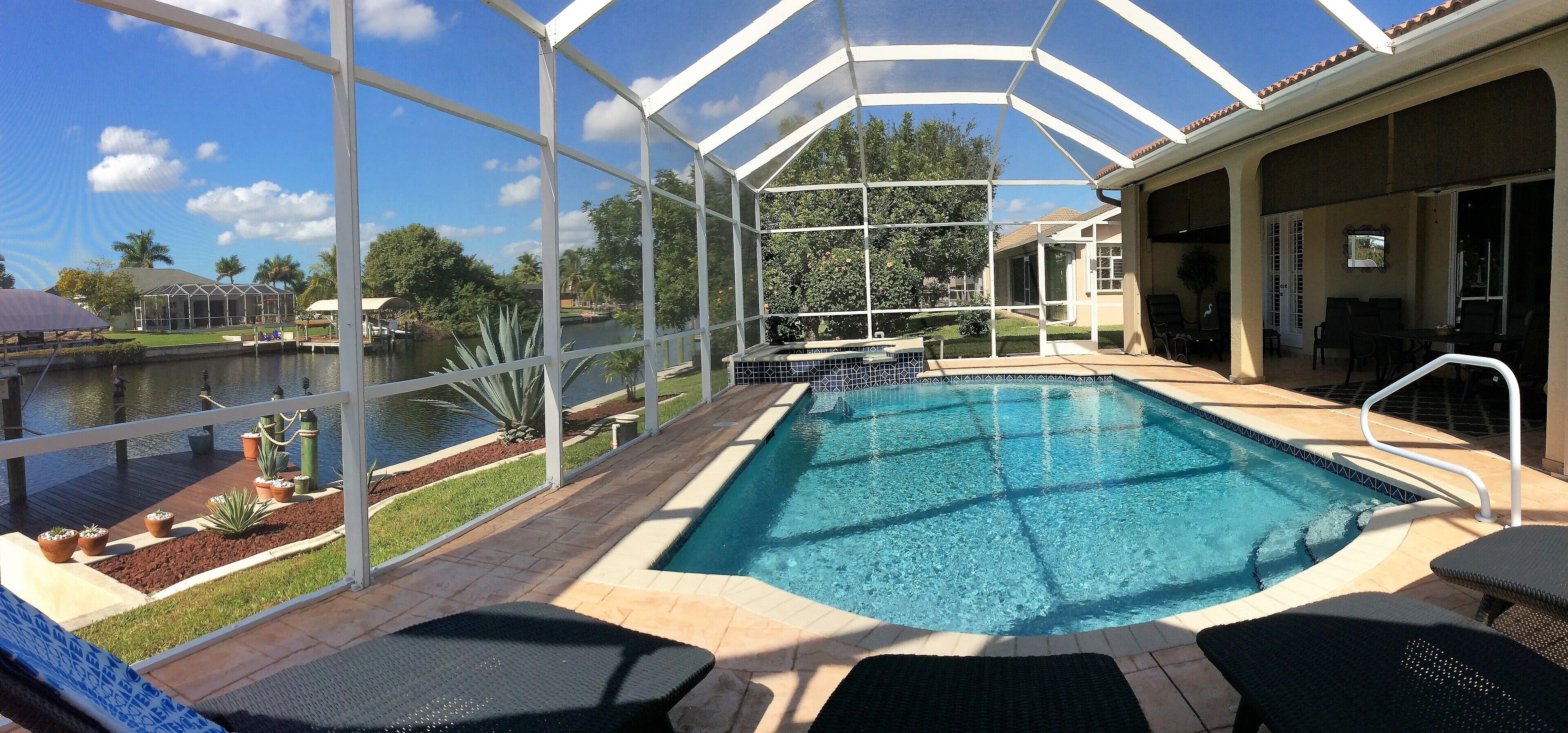 A pool area with a glass enclosure, a pool, and a patio with chairs and a table.