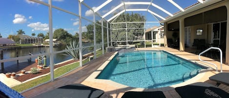 A pool area with a glass enclosure, a pool, and a patio with chairs and a table.