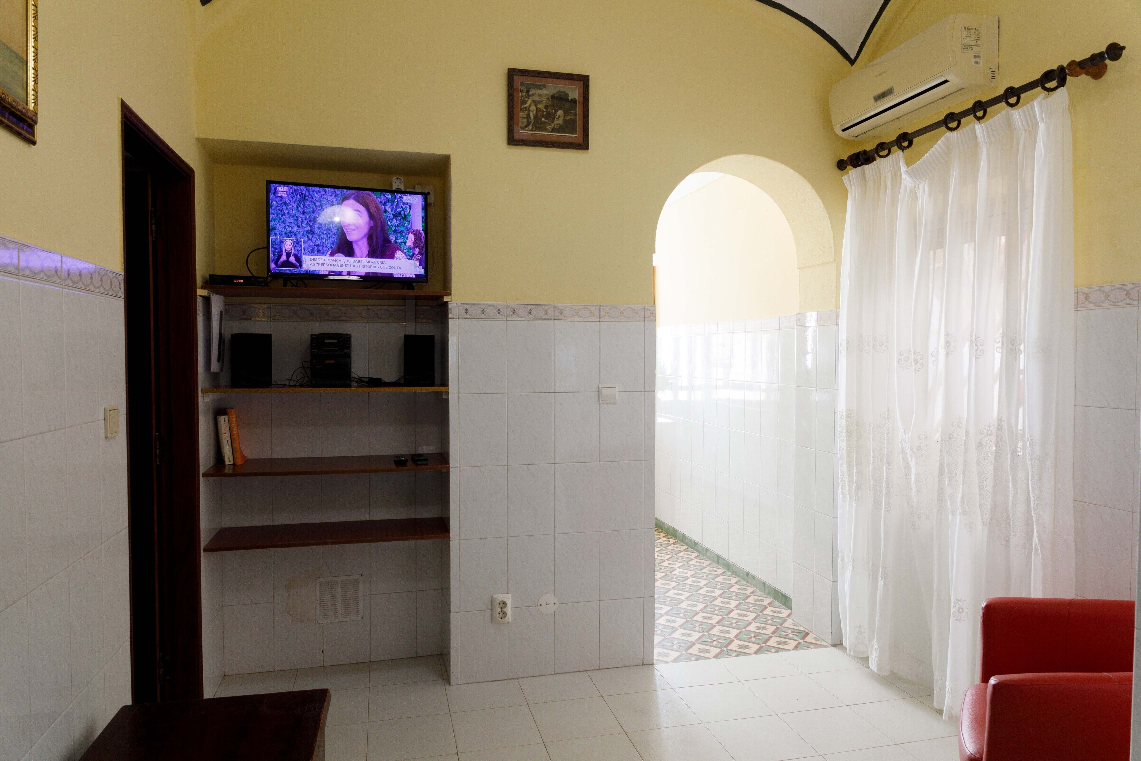 Ein Hotelzimmer mit Fernseher auf einer Ablage, einem roten Sessel und Blick auf einen gefliesten Innenhof.
