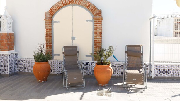 A terrace with two lounge chairs and two potted plants, a white wall with a brick archway, and a tiled floor. - House / Villa - Fuseta (Fuseta)