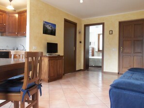 A kitchen with wooden cabinets, a dining table, and a TV on a stand. - Apartment/ flat - Saint-Pierre (Saint-Pierre)