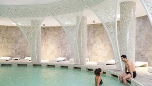 Une piscine intérieure au design moderne, avec des motifs géométriques sur le plafond et les murs, et un espace de détente minimaliste et épuré autour de la piscine, agrémenté de chaises longues.