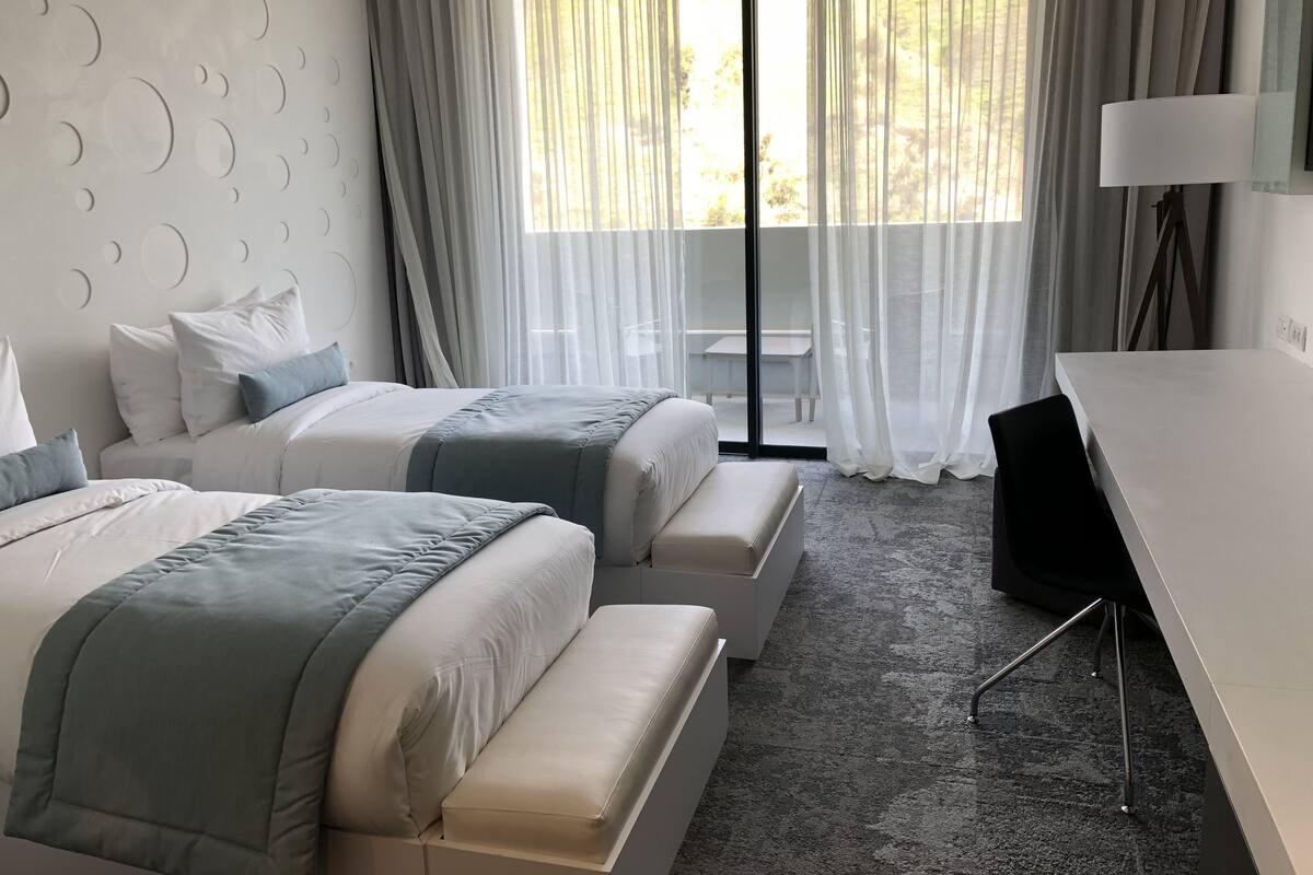 A modern hotel room with two beds, a desk, and a balcony.