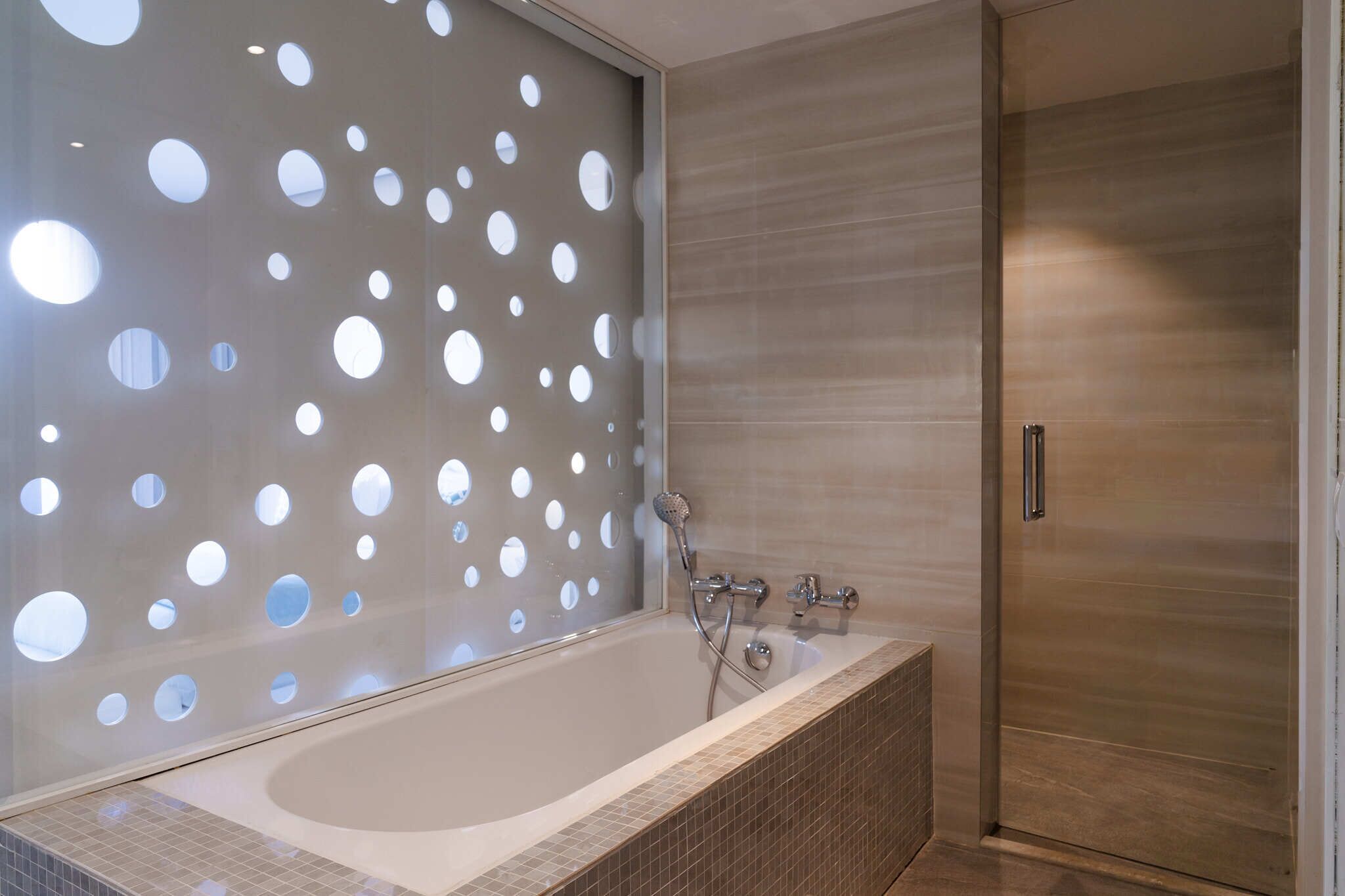 A modern bathroom with a freestanding bathtub, a shower with a handheld showerhead, and a wooden door.