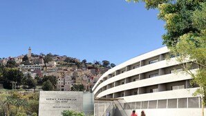 Un hôtel moderne à la façade incurvée, une enseigne indiquant qu’il s’agit de l’hôtel-spa Vichy Thermalia à Moulay-Yacoub, et une vue sur une ville située sur une colline en arrière-plan.