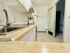 Uma cozinha com pia de aço inoxidável, armários brancos, micro-ondas e painel de azulejos.