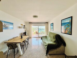 Una habitación con una mesa de comedor, sillas, un sofá, un televisor y un balcón con vistas.