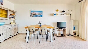 Een eetgedeelte met een houten tafel, stoelen, een televisie en een boekenkast.