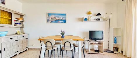 Un coin repas avec une table en bois, des chaises, un téléviseur et une bibliothèque.