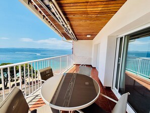 Uma varanda com mesa e cadeiras, vista para o mar e teto de madeira.